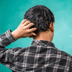Back view of a student scratching his head in confusion, wearing a checkered shirt and standing against a teal background.