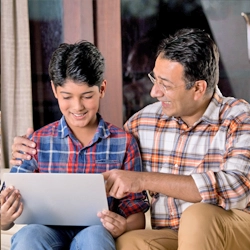 A smiling father and son sitting together, looking at a tablet or laptop screen, engaged in an educational or fun activity.